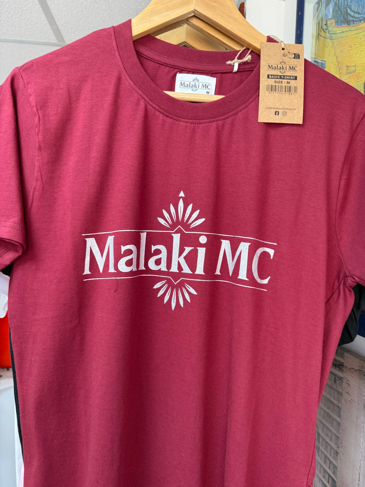 Malaki MC burgundy t-shirt on hanger with branded tag showing logo detail